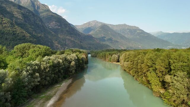 A fast drone flyover of the Toce River, framed by trees, with mountains and sky in the background, showcasing the stunning landscape of Ansola, Italy.