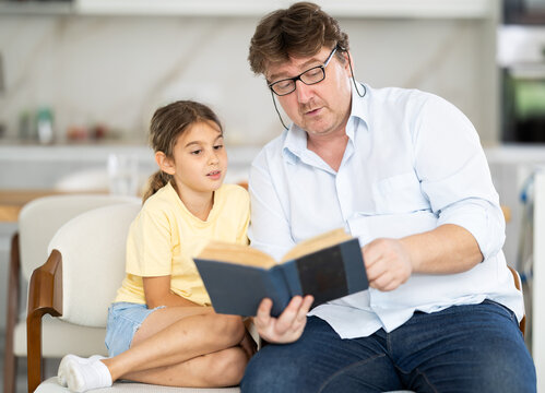 Father reads book to little cute daughter, spend leisure enjoy good life hobby and pastime at home. Fatherhood, upbringing, children development