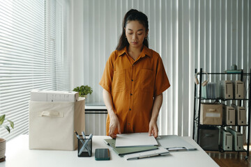 Young pregnant woman standing over desk in office carefully organizing documents and focusing on...
