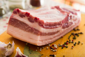 Fresh piece of pork belly on wooden board with spices