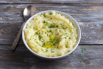 Mashed potatoes with melted butter and herbs in a gray ceramic bowl on a wooden table