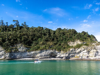 Obraz premium Panoramic view of a coastal landscape with cliffs and the sea being crossed by a small pleasure boat on a sunny day. Plencia, Bizcay