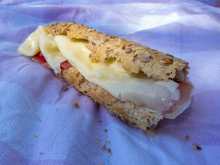 Close-up detail of a delicious Serrano ham and cheese sandwich on cereal bread on a chequered towel at a picnic.