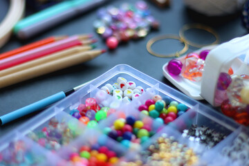 Colorful beads, coloring pencils, glitter, needles, string, hoop, tape and scissors on dark background. Various colorful craft supplies. Selective focus.