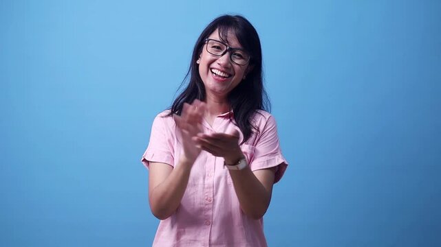 Smiling charming Asian woman claps hands, congratulating. Support, cheering, bravo. Isolated on blue background