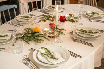 Festively decorated dinner table set for a Christmas celebration, with lit candles, fresh greenery, and seasonal decorations, exuding a warm and inviting holiday ambiance