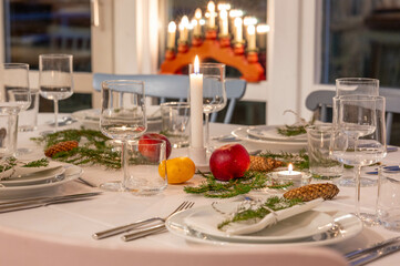 Festively decorated dinner table set for a Christmas celebration, with lit candles, fresh greenery, and seasonal decorations, exuding a warm and inviting holiday ambiance