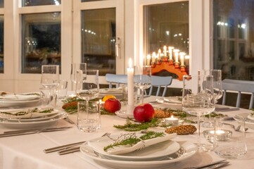 Festively decorated dinner table set for a Christmas celebration, with lit candles, fresh greenery, and seasonal decorations, exuding a warm and inviting holiday ambiance