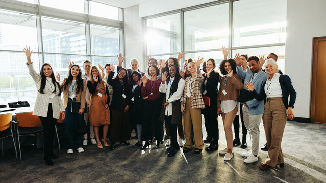 Diverse group at seminar happily waving inside modern conference room with large windows and bright natural light