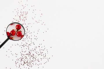 Looking through a magnifying glass on a red Christmas ball over a gliitter on a white background. Christmas time idea, holiday decoration concept. Copy space.