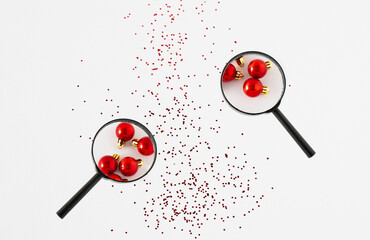 Looking through a magnifying glass on a red Christmas ball over a gliitter on a white background. Christmas time idea, holiday decoration concept. 