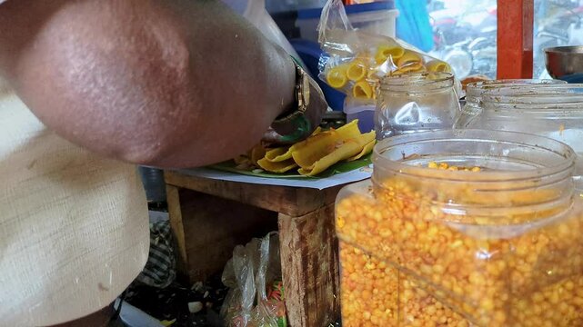 A man preparing boti masala chaat or crunchy finger fryums with salad and chutneys