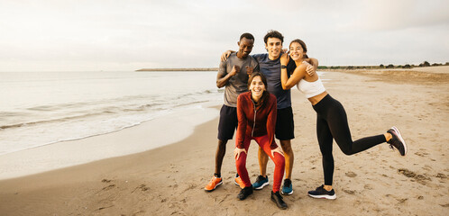 Group picture of cheerful friends exercising together on a beach, embracing fitness and friendship in a lively setting during the morning.