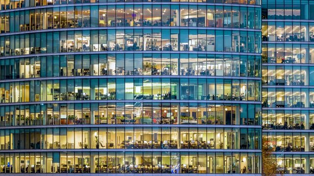 Timelapse panning view of an illuminated office building during evening with workers movement