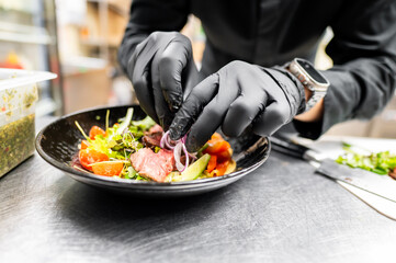 A chef in a professional kitchen garnishing a gourmet salad with fresh herbs. The focus is on the chef’s hands and the dish, highlighting the culinary presentation and attention to detail