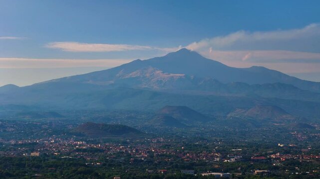 Aerial pull-back view of Mount Etna in Sicily with smoke from the crater and small villages in the foothills