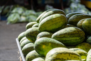 Watermelons - green tropical fruit with pink red flesh centre, stacked on table at fresh produce...
