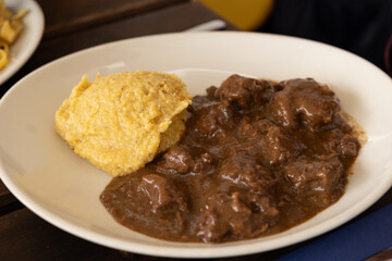 piatto con pezzetti di carne di manzo, cotta, con sugo e polenta