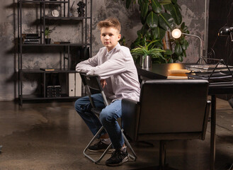 A young boy sits calmly in a stylish office, deep in thought, with a well-organized desk and vibrant plants enhancing the serene atmosphere of the creative space.