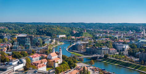 Obraz premium Aerial view of Vilnius, Lithuania, featuring Gediminas' Tower on a green hill, the Neris River, and a mix of modern and traditional architecture.