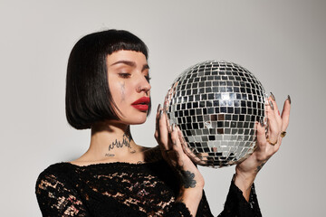 Naklejka premium Stylish woman with tattoos showcases a sparkling disco ball in a chic environment.