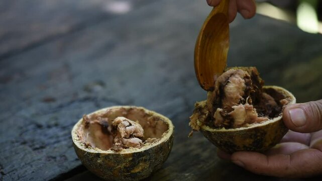 A man is using a spoon to scoop up Limonia or Feronia limonia (L.) Swingle fruit pulp on an old wooden background.