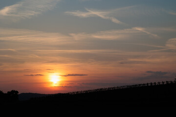 sole che tramonta dietro la sagoma di una collina e colora di arancione le nuvole leggere e la foschia nel cielo