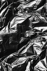 Vertical A close-up of a wrinkled plastic and foil texture, featuring crumpled patterns and a mix of silver and black hues.