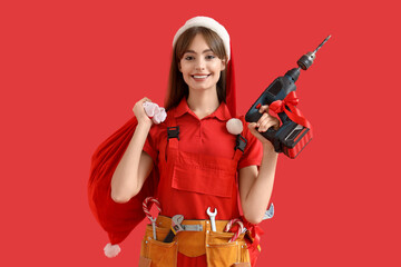 Female worker in Santa hat with bag of gifts and drill on red background