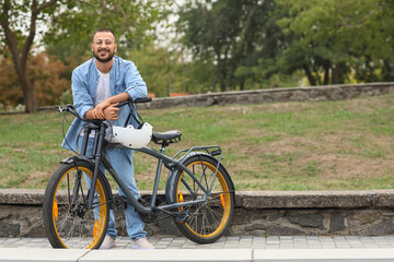 Young happy man with helmet and bicycle walking in park on autumn day