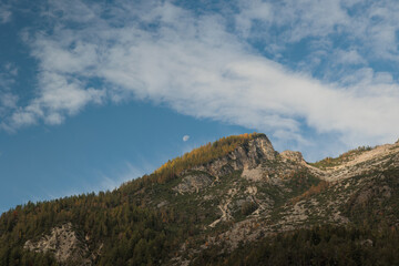 dettaglio di un'alta catena montuosa rocciosa e coperta in parte dalla vegetazione e da foreste, sotto un cielo parzialmente nuvoloso in autunno