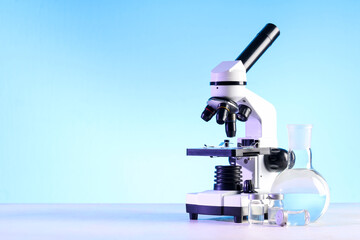Modern microscope, ampules and laboratory flask with liquid on white table
