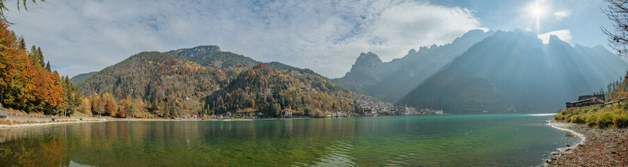 Fototapeta premium composizione panoramica con vista sul Lago di Alleghe, nel Veneto nord-occidentale, di giorno, sotto un cielo leggermente nuvoloso, in autunno