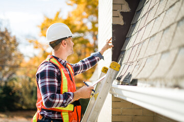 man with hard hat standing on steps inspecting house roof