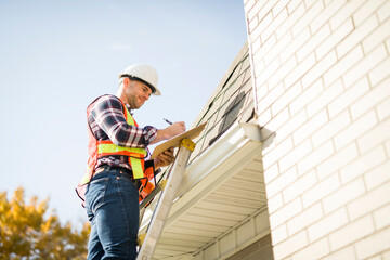 man with hard hat standing on steps inspecting house roof