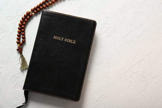 Holy Bible with rosary beads on light background