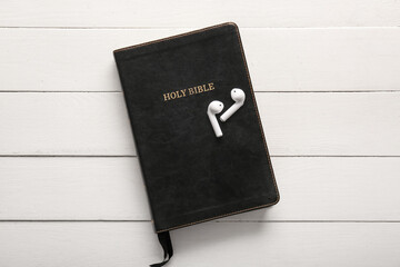 Holy Bible and earphones on white wooden background