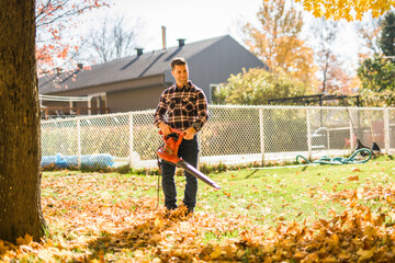 A Man cleaning fallen leaves using a leaf blower on the lawn.