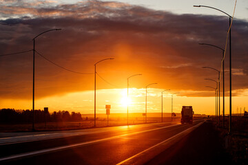A truck is driving down the road into an orange sunset