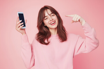 Fototapeta premium Vibrant Fashionista in Pink Smiles Brightly in Studio Portrait , A woman invites you to look at a product on a mobile phone screen.