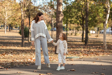Happy mother with her cute little daughter walking in beautiful autumn park