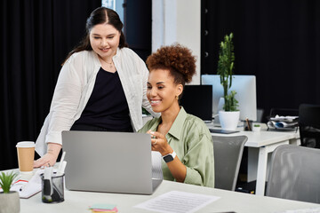 Two professional women engage in a collaborative discussion while working on a laptop.