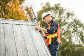 man with hard hat standing on steps inspecting house roof