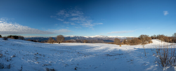 ampia composizione panoramica di un ambiente che si estende tra le colline e le montagne innevate...