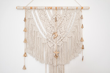 Macramé wall hanging with wooden embellishments displayed on a white wall
