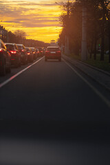 Autumn landscape and view of the road with cars. Orange evening sun and reflections on cars.