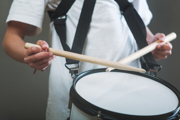 Hands of an unrecognizable young person holding a pair of drumsticks and playing a white drum