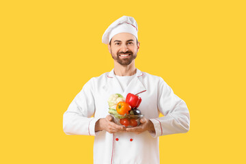 Handsome bearded chef with fresh vegetables on yellow background