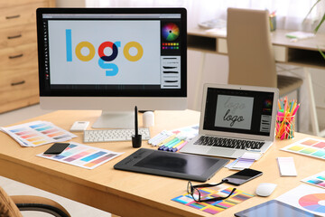 Workspace of graphic designer with modern computer, tablet, laptop and color palettes in office