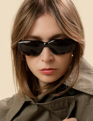 Naklejka premium Portrait of young modern woman in green trench coat, tortoise shell sunglasses and curtain bangs